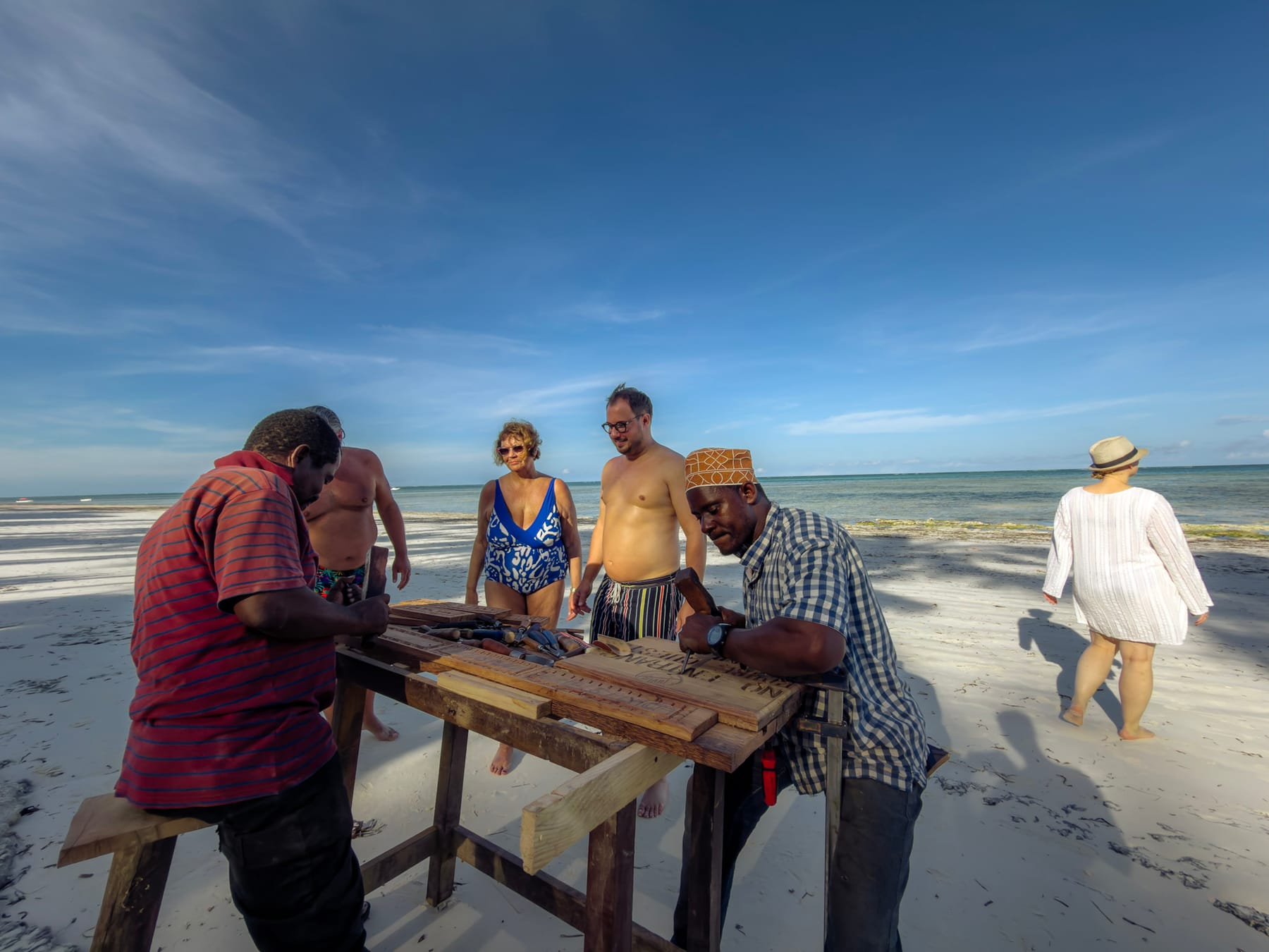 Craftsman carving wood on a Zanzibar beach with visitors watching